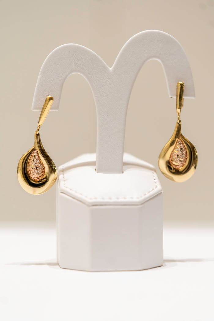 Home Luxurious gold earrings beautifully displayed on a white stand in a well-lit environment.