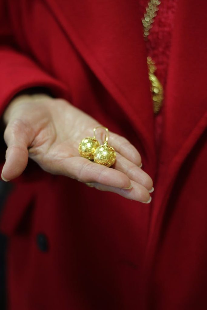 Mastering the First Impression: Your intriguing post title goes here Close-up of a pair of exquisite gold earrings presented in hand against a red background.