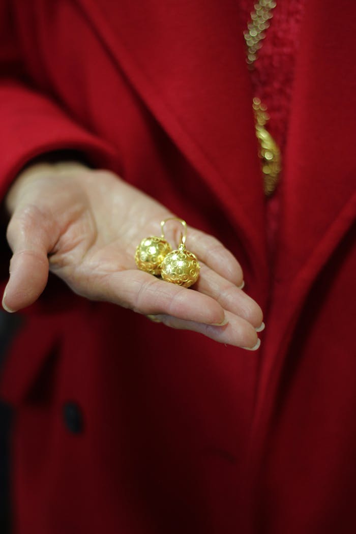 Close-up of a pair of exquisite gold earrings presented in hand against a red background.