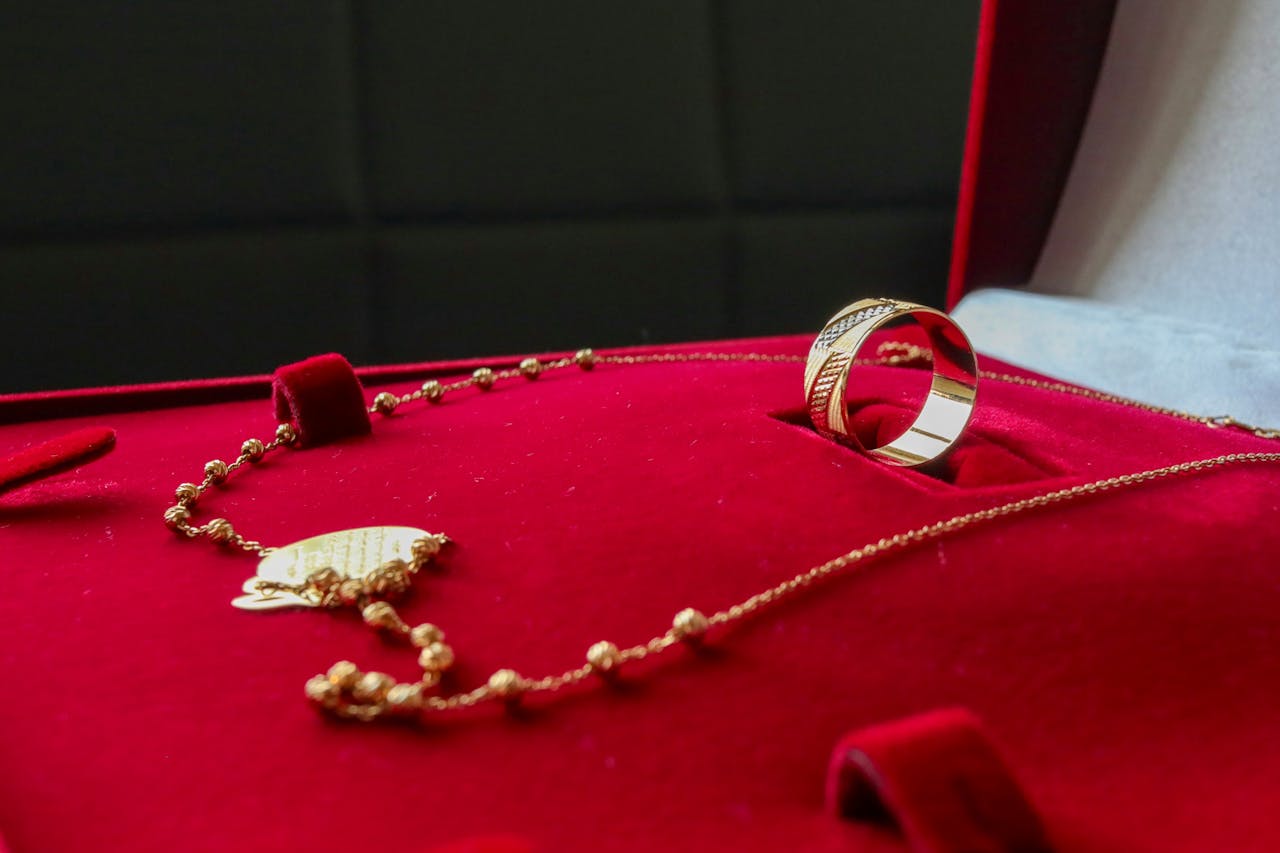 Services Gold necklace and ring elegantly displayed on rich red velvet background, highlighting luxury and elegance.