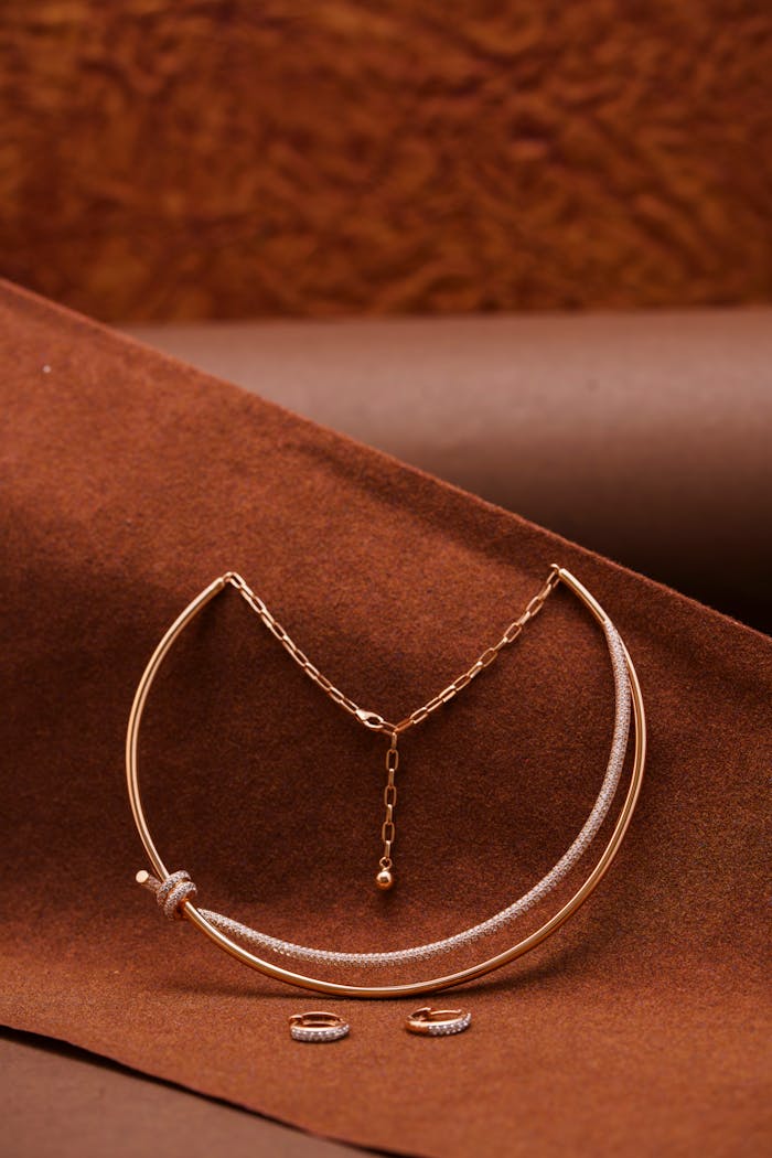 Services Stylish rose gold necklace and rings on textured brown fabric backdrop perfect for fashion advertising.