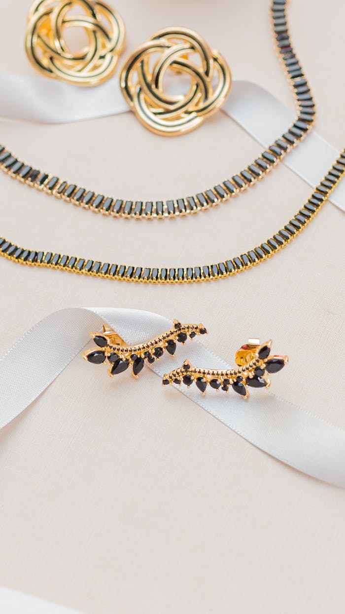 Home A sophisticated gold jewelry set displayed on a white ribbon, highlighting elegance and luxury.